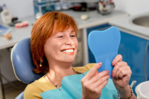 a woman holding up a mirror and smiling with her new dental implants